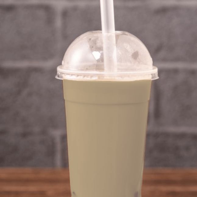 A glass of brown drink with tapioca pearls on top, set against a grey brick background.