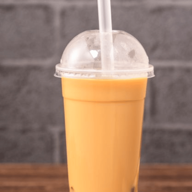 A plastic cup filled with a colorful bubble tea drink, topped with black tapioca pearls, on a grey brick background.